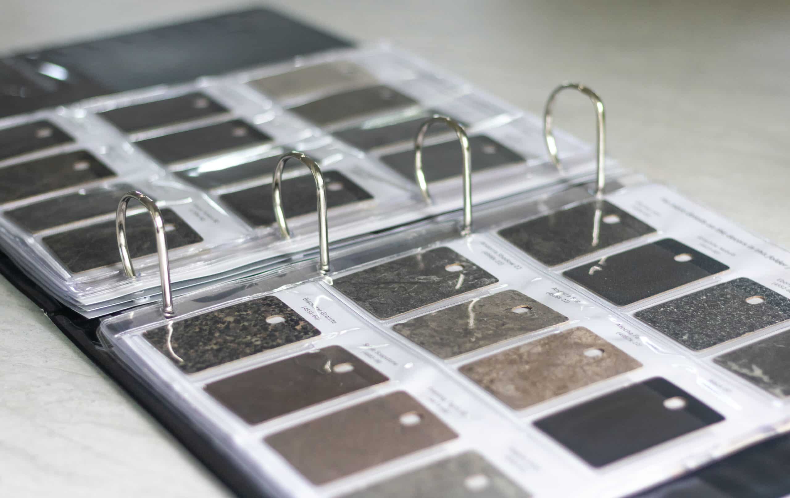 En pärm med olika stenprover används för att välja material vid renoveringar. Pärmen ligger på ett bord och innehåller etiketter för varje sten, lämpliga för Clas Fixare:s hantverkstjänster.